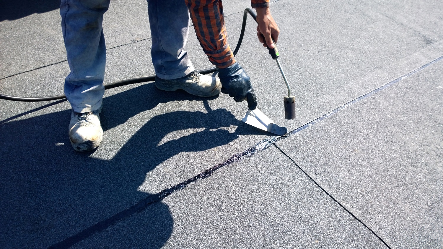 Roofer preparing part of bitumen roofing felt roll for melting by gas heater torch flame